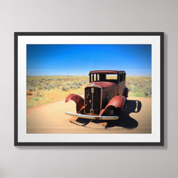 An antique car with rusted red fenders and a desert landscape in the background, photographed on historic Route 66 near Holbrook, Arizona, under a bright blue sky.