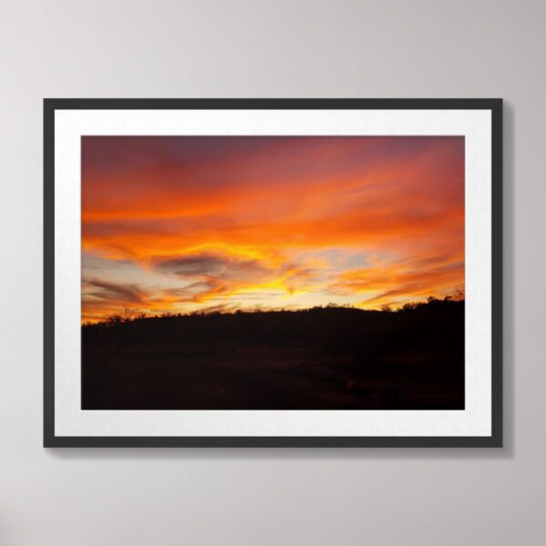 A vivid Arizona sunset with fiery orange, red, and golden hues lighting up the sky over a rugged desert landscape in Southwestern Arizona.