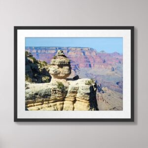 A vibrant photograph of Duck Rock, a unique rock formation perched on the edge of the Grand Canyon, with layers of red and orange cliffs in the background.