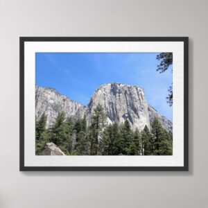 A stunning view of El Capitan, a granite monolith in Yosemite National Park, surrounded by a lush forest and under a bright blue sky.