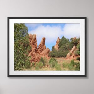 A vibrant photograph of the red rock formations at Garden of the Gods in Colorado Springs, Colorado, framed by lush greenery and a blue sky with soft clouds.