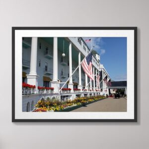 Framed art print of the Grand Hotel on Mackinac Island, Michigan, featuring iconic white columns, vibrant flowers, and American flags against a blue sky.