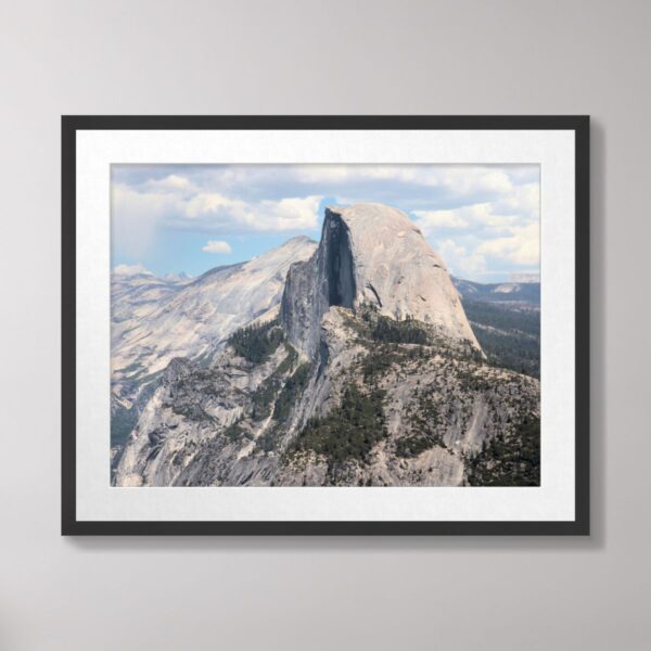 A closeup view of Half Dome’s granite face and rugged surroundings under a bright sky at Yosemite National Park.