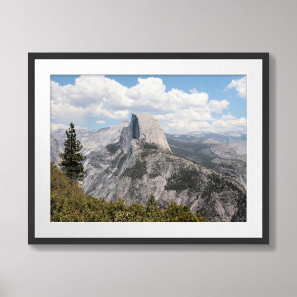 A stunning view of Half Dome rising above the forested landscape in Yosemite National Park, framed by a clear blue sky and fluffy white clouds.