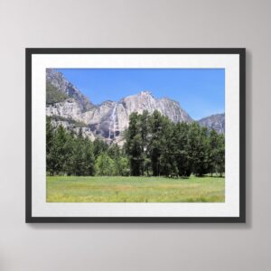 A stunning view of Yosemite Falls cascading down granite cliffs, surrounded by lush green meadows and framed by trees at Yosemite National Park under a clear blue sky.