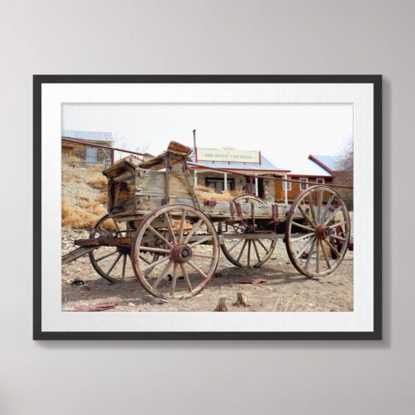 A weathered antique wooden wagon in the ghost town of Belmont, Nevada, with historic buildings and desert scenery in the background.