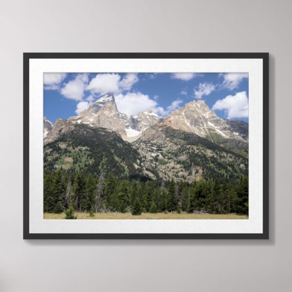 The Grand Teton Mountains in Grand Teton National Park with lush green forests and a bright blue sky with clouds.