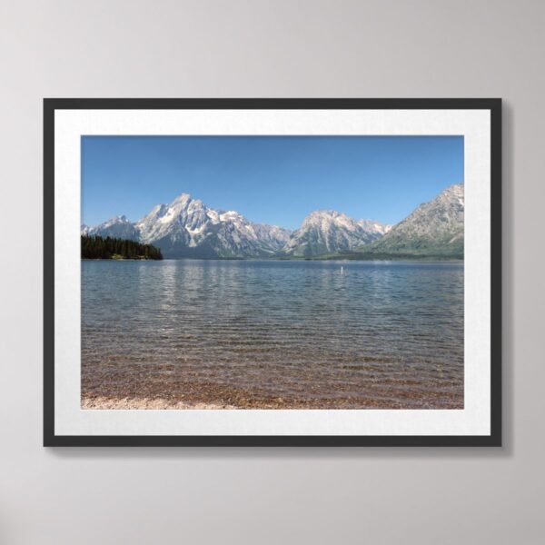 A scenic view of Jackson Lake at Grand Teton National Park with the majestic Teton mountain range reflected on the lake's crystal-clear waters and a rocky shoreline in the foreground.