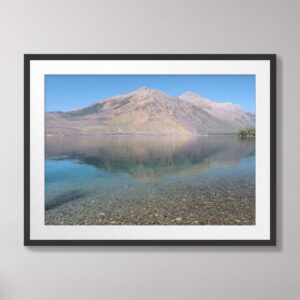 A serene view of Lake McDonald at Glacier National Park with clear waters reflecting the surrounding mountains under a bright blue sky.