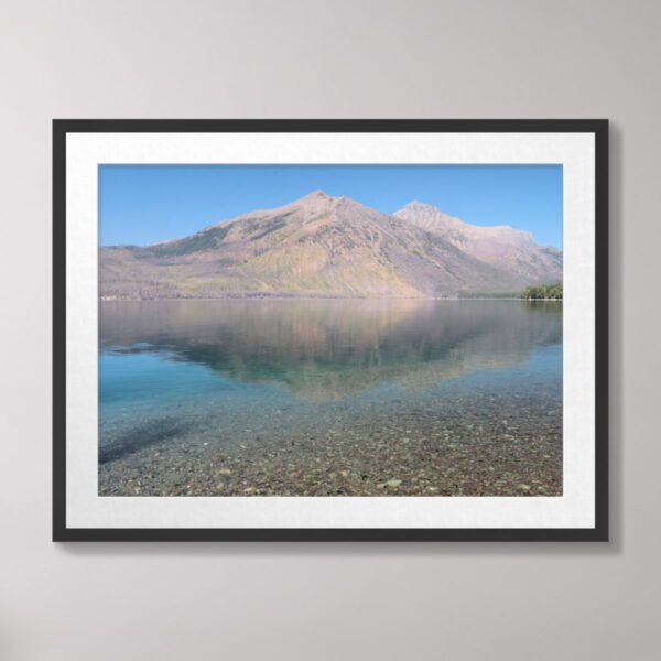 A serene view of Lake McDonald at Glacier National Park with clear waters reflecting the surrounding mountains under a bright blue sky.