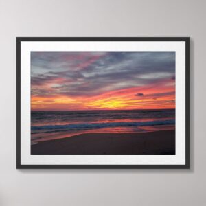 Photograph of a vibrant sunrise over the beach in Kitty Hawk, North Carolina, featuring vivid pink, orange, and purple hues reflecting on the ocean and sand.