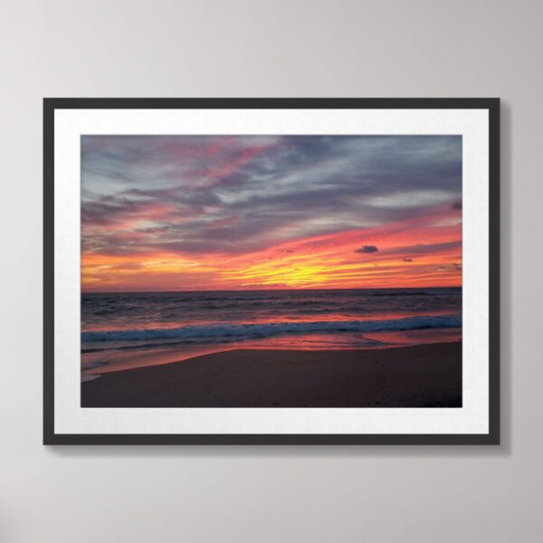 Photograph of a vibrant sunrise over the beach in Kitty Hawk, North Carolina, featuring vivid pink, orange, and purple hues reflecting on the ocean and sand.