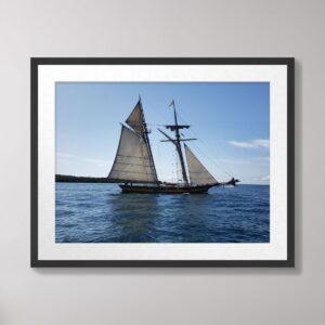 A schooner with full sails gracefully sailing on the calm waters of Lake Huron near Mackinac Island under a clear blue sky.