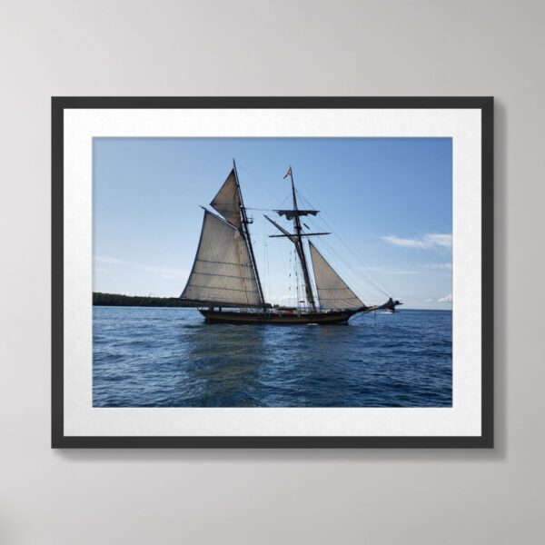 A schooner with full sails gracefully sailing on the calm waters of Lake Huron near Mackinac Island under a clear blue sky.