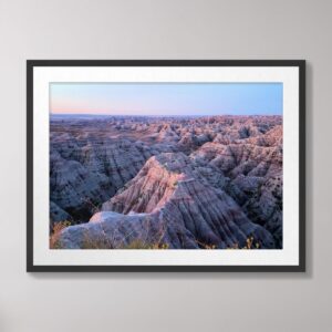 A stunning photograph of the sunrise over the rugged geological formations of Badlands National Park, South Dakota, with layers of pink and lavender hues reflecting off the dramatic terrain.