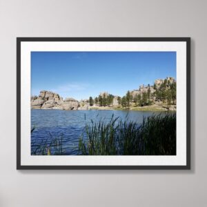 A serene photograph of Sylvan Lake at Custer State Park, South Dakota, featuring calm waters, lush greenery, and dramatic rock formations under a vibrant blue sky.