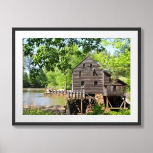 Photograph of Yates Grist Mill in Raleigh, North Carolina, surrounded by lush greenery, with its reflection visible in the calm waters below.