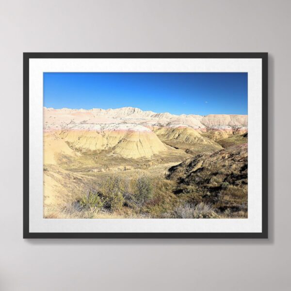 A colorful photograph of the Yellow Mounds at Badlands National Park, South Dakota, featuring layers of yellow and pink sediment beneath a clear blue sky.