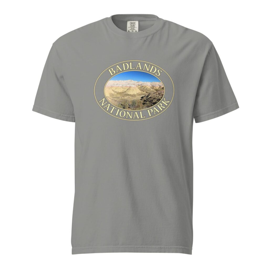 Grey Comfort Colors heavyweight T-shirt featuring a scenic Yellow Mounds design at Badlands National Park, framed in an oval border.