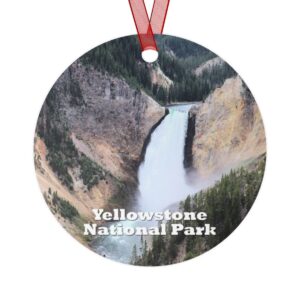 A 3.5-inch aluminum ornament featuring a vivid image of the Lower Yellowstone Falls surrounded by rugged cliffs and evergreen trees. Includes a red ribbon for hanging.