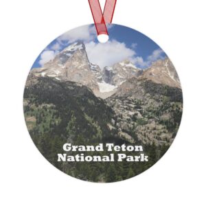 A 3.5-inch aluminum ornament featuring the striking Grand Teton Mountains against a blue sky with lush greenery in the foreground. Includes a red ribbon for hanging.